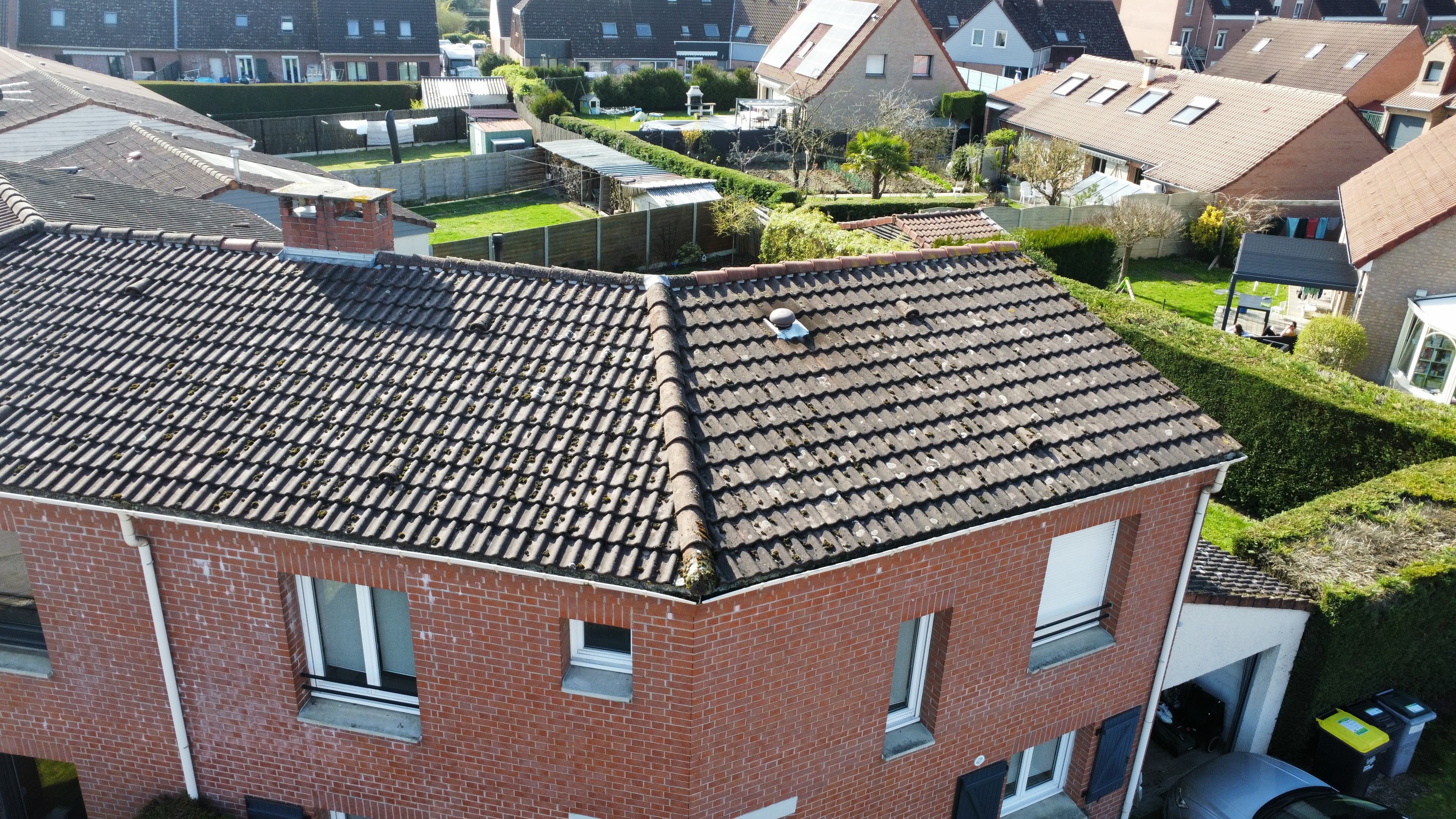 Vue aérienne d'une maison en briques rouges avec toit en tuiles dans un quartier résidentiel.