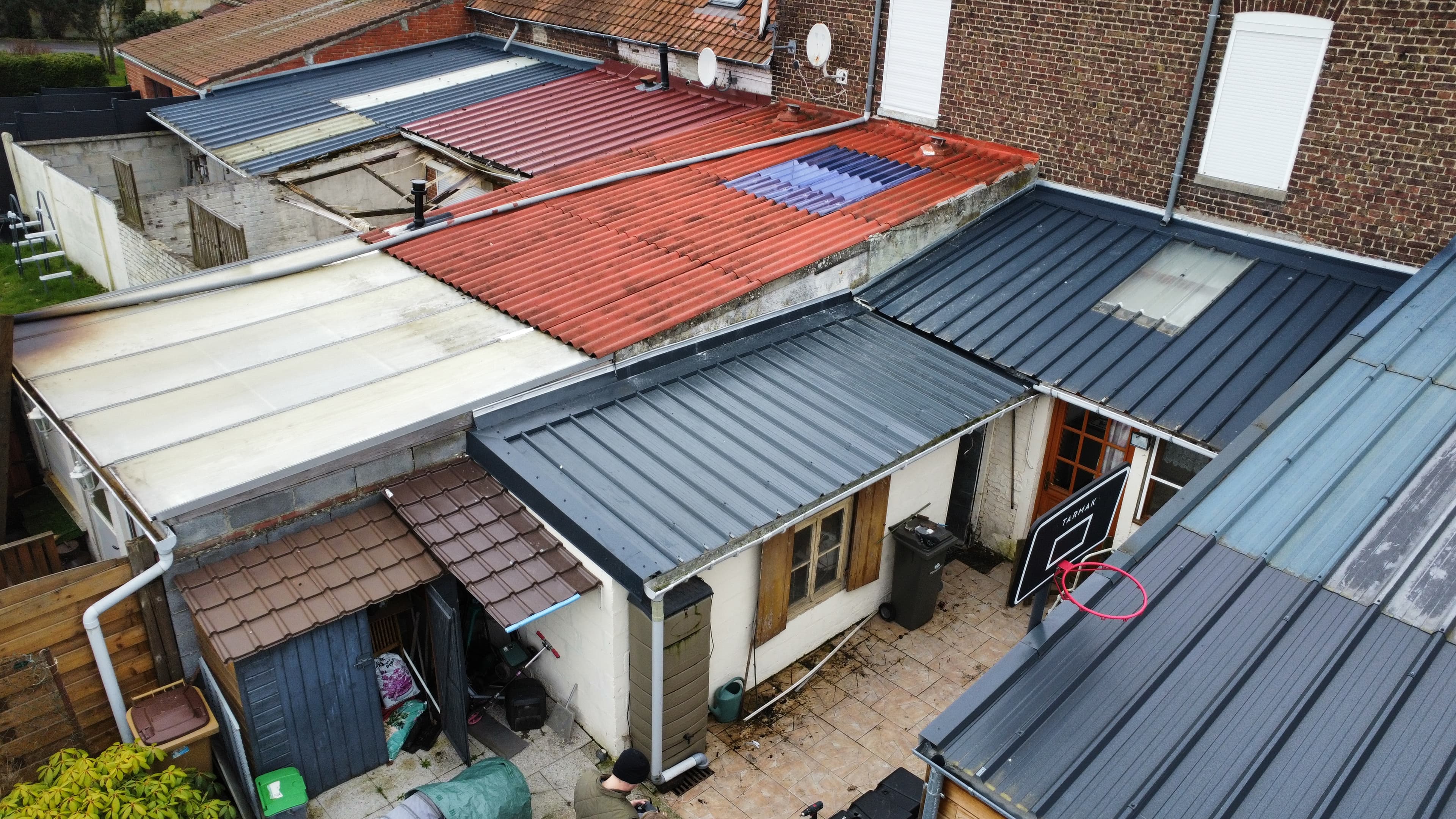 Toitures en tôle et tuiles surplombant une petite cour avec un panier de basket.